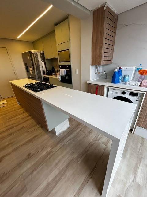 Ilha de cozinha com bancada branca e área de serviço integrada.